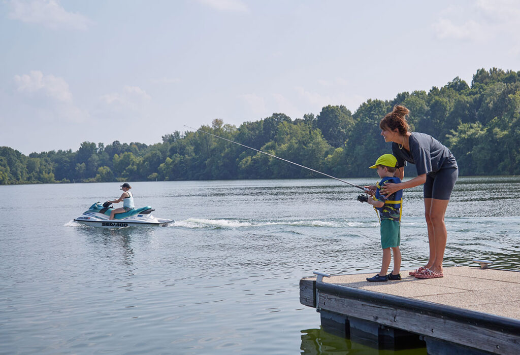 Women and boy pier fishing while jet-skier drives by